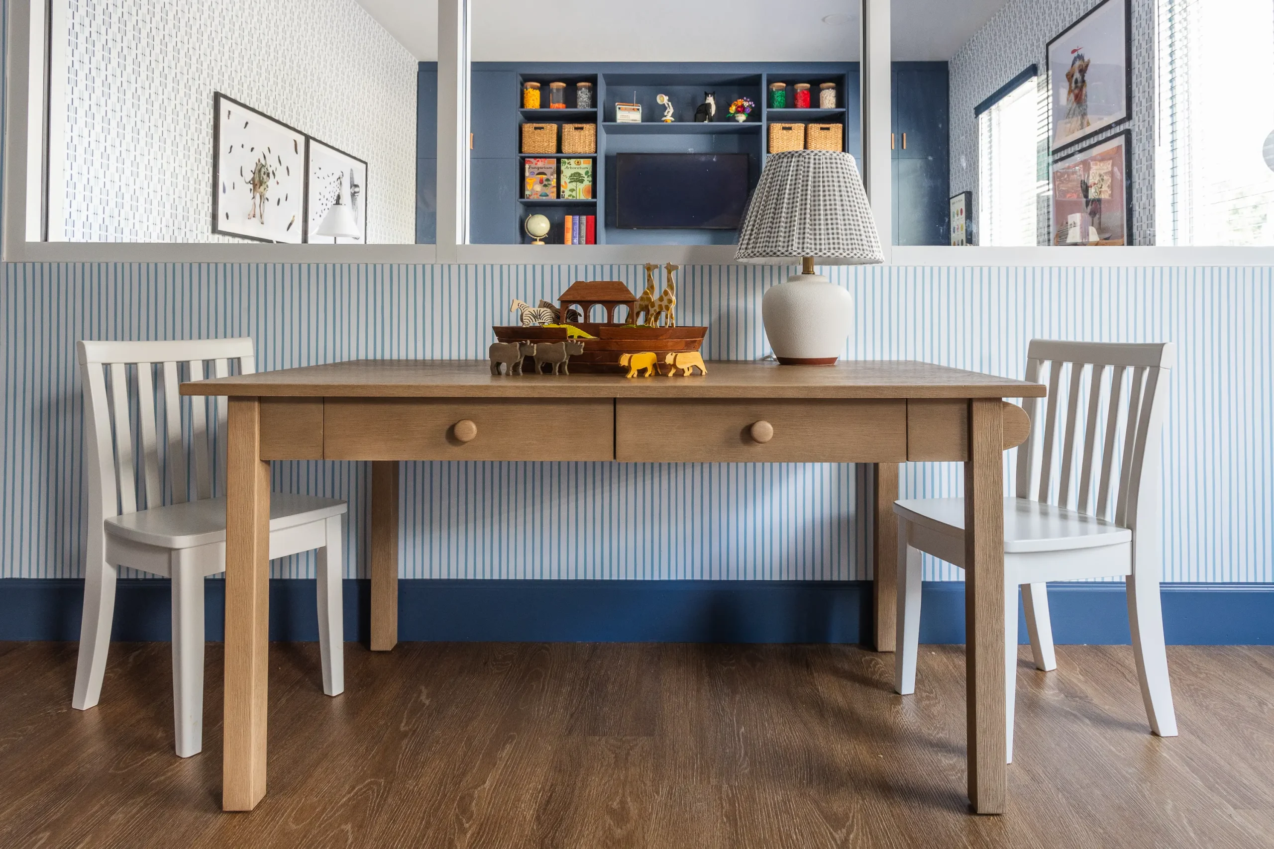 Child-sized wooden activity table with two white chairs and a Noah's ark toy set, against blue striped wainscoting
